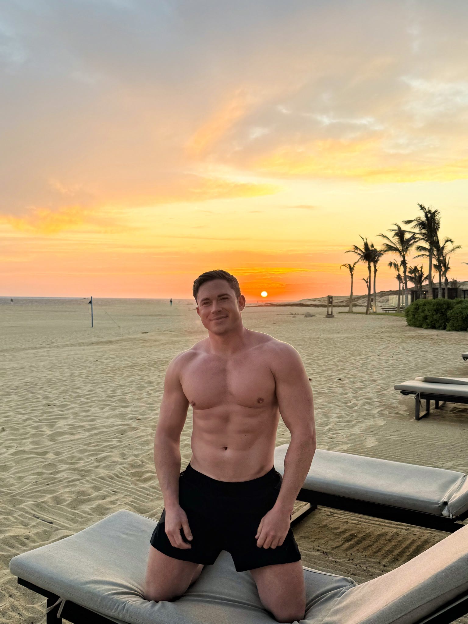 Will Parfitt kneeling on a sun lounger on an empty beach at sunset